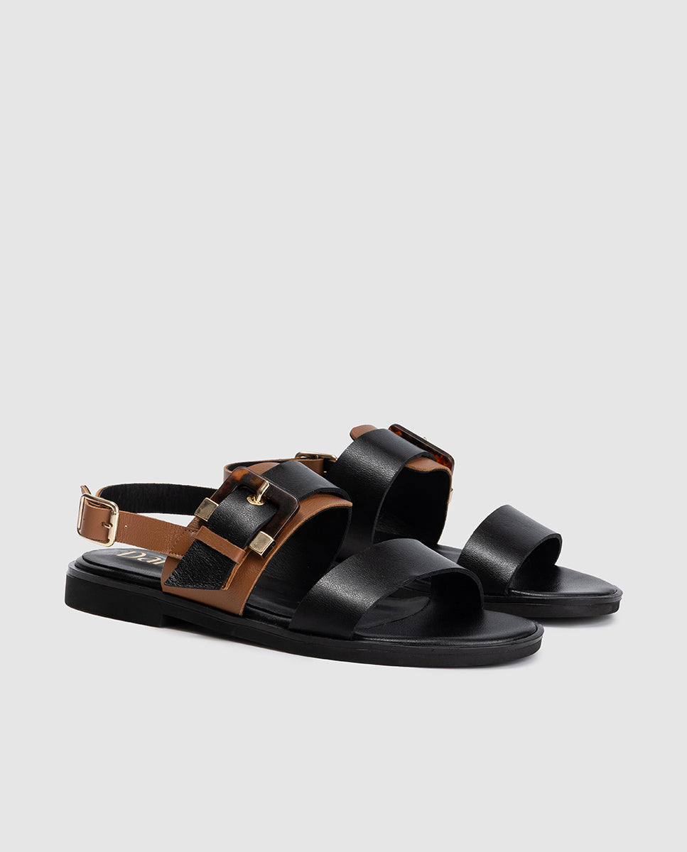 Vista frontal 3/4 de sandalia plana bicolor en piel napa negra y cuero con gran hebilla carey modelo Abi Dansi