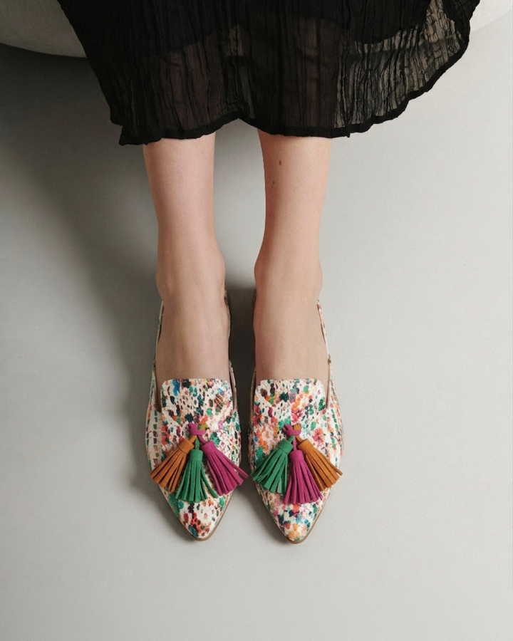 Modelo con vestido negro y zapatos planos destalonados estampado multicolor con borlas de Dansi